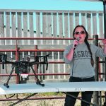 U of S master’s student Alex Waldneruses a microphone to address a group with a drone sitting on the table in front of her.