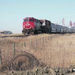 A grain train moves slowly down the tracks past an inland elevator facility in Saskatchewan.