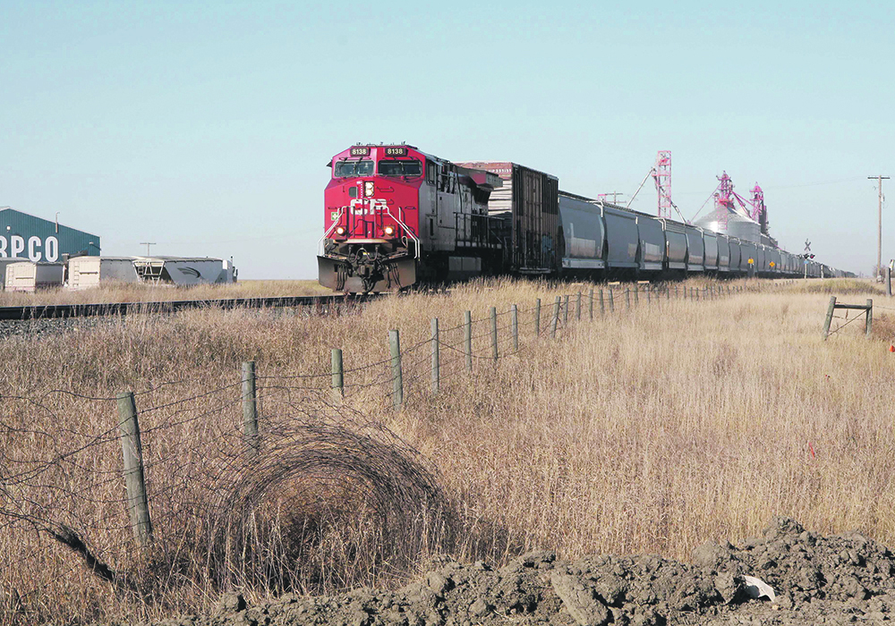 A grain train moves slowly down the tracks past an inland elevator facility in Saskatchewan.