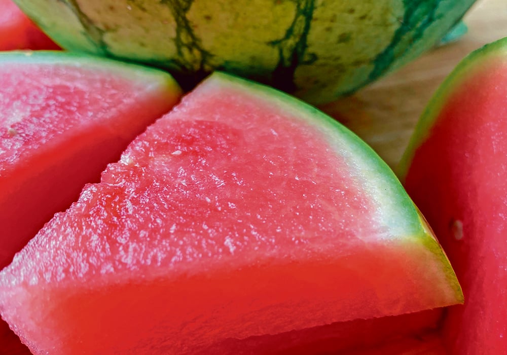 Several juicy, red triangular wedges of watermelon sit on a table in front of a half of the remaining melon.