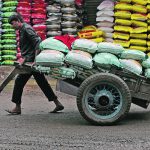 A labourer pulls a hand cart loaded with sacks of lentils in an Indian market.