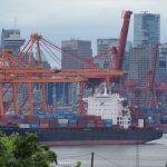 A container ship is underway in the Port of Vancouver with the city's downtown skyline in the background.
