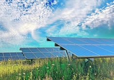 A large solar array sits in a field under a mostly cloudy sky.