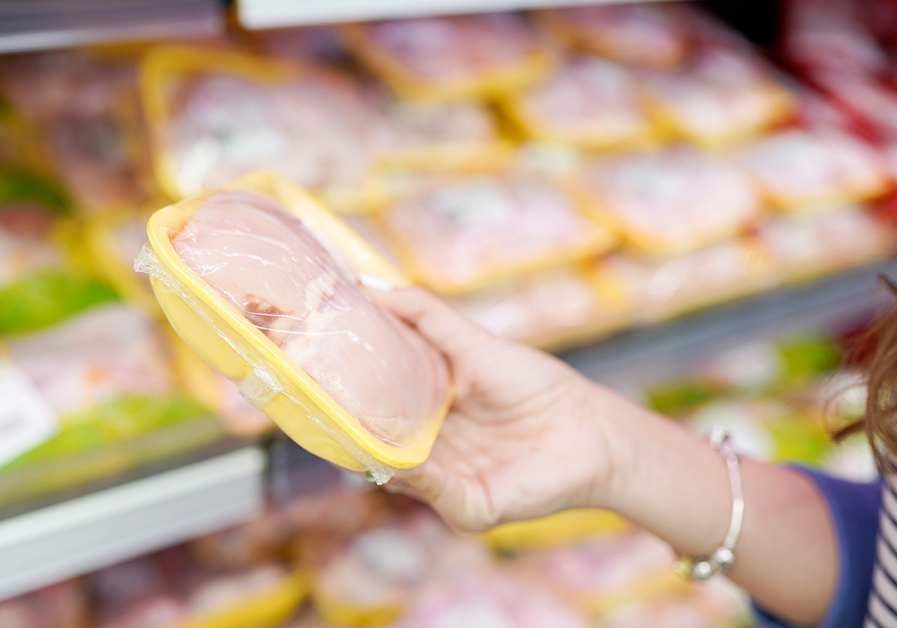 Close-up of two packaged chicken breasts being held in a woman's hand in a grocery store.