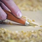 Close-up of a hand holding precision knife to cut a wheat kernel.