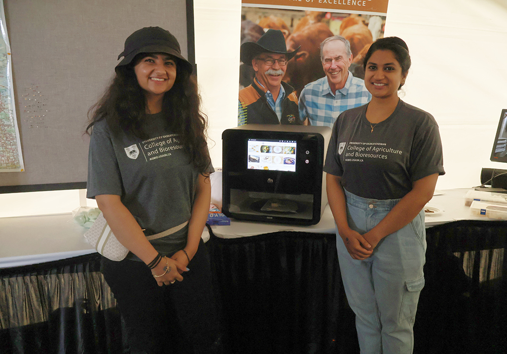 Kashika Sethi (left) and Rhea Thomas Thommana (right) were at Ag in Motion to represent the Department of Food and Bioproduct Science, and to show some of the ongoing projects at the University of Saskatchewan including the pea-based “chicken leg” seen in the machine.