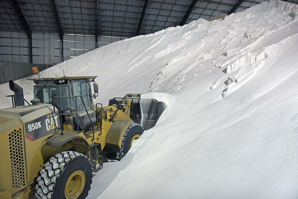 A payload scoops a bucket full of white fertilizer from a large pile.