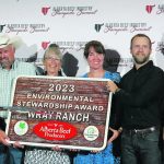 The Wray family holds up a carved wooden sign: "2023 Environmental Stewardship Award: Wray Ranch"