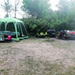 a campsite with a screen tent and car parked to the side.