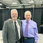 two elderly men smile as they pose for a picture at a convention centre