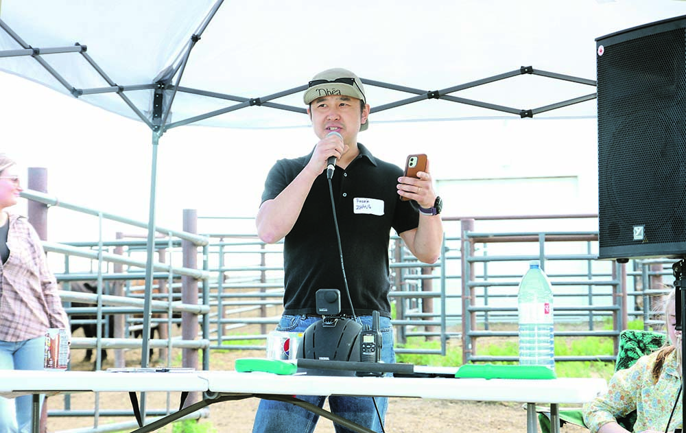 A man in a baseball cap speaks into a microphone with cattle pens in the background