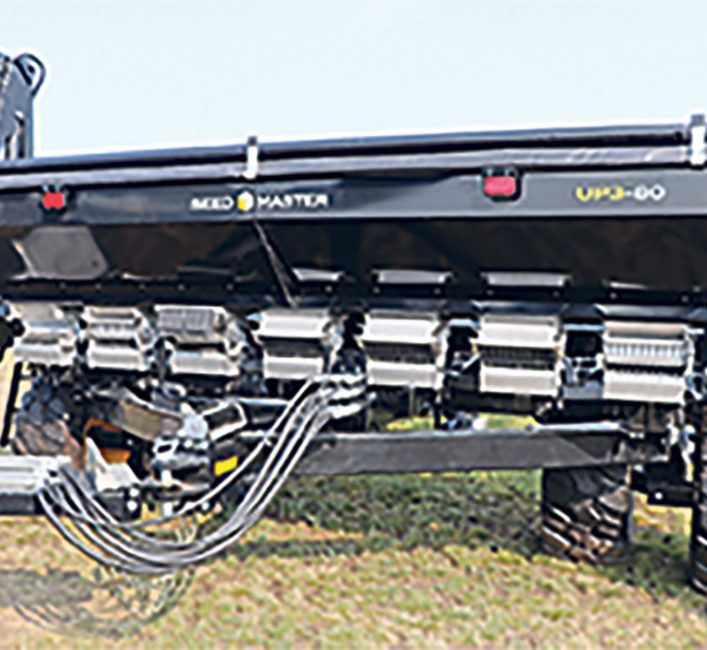 The hitch of an air seeder, showing the tank above and seven stainless steel boxes and a bundle of black hydraulic hoses