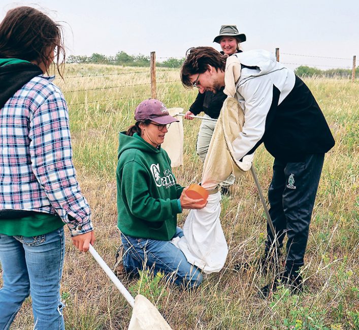 A woman holding a white bak while a man shakes out a collection net into it while a young girl approaches with another net.