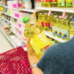 A shopper holds a bottle of vegetable oil in an aisle in a supermarket.