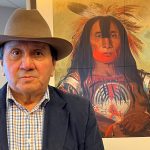 Kainai-Blood Chief Roy Fox (Blackfoot name Makiinima) stands in front of a painting of Stamikso’sak, a Blood Tribe war chief from the early 1800s. | Supplied photo