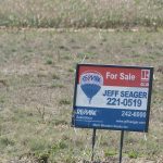 A realtor's "for sale"sign sits on the edge of a field.