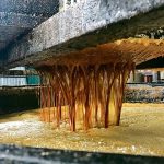 Close-up photo of the surface of a giant vat of used cooking oil with more pouring in through some kind of strainer above.