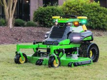 A John Deere autonomous, battery-electric, zero-turn mower sits on some grass.