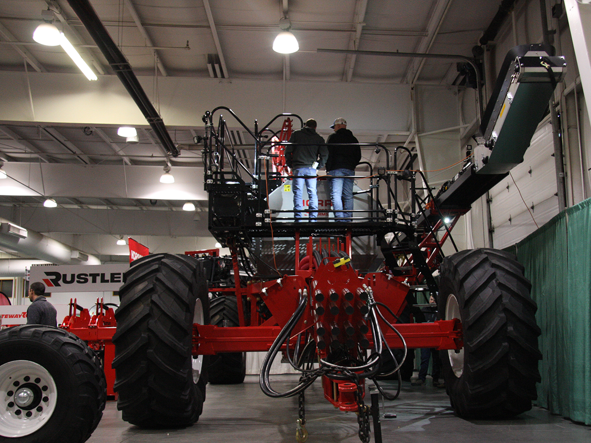 Two men stand on top of a large red piece of farm machinery - a Morris Series 10 air cart - at the 2025 Crop Production Show in Saskatoon.