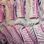 Two rows of sides of beef hang in a large refrigerated meat locker.