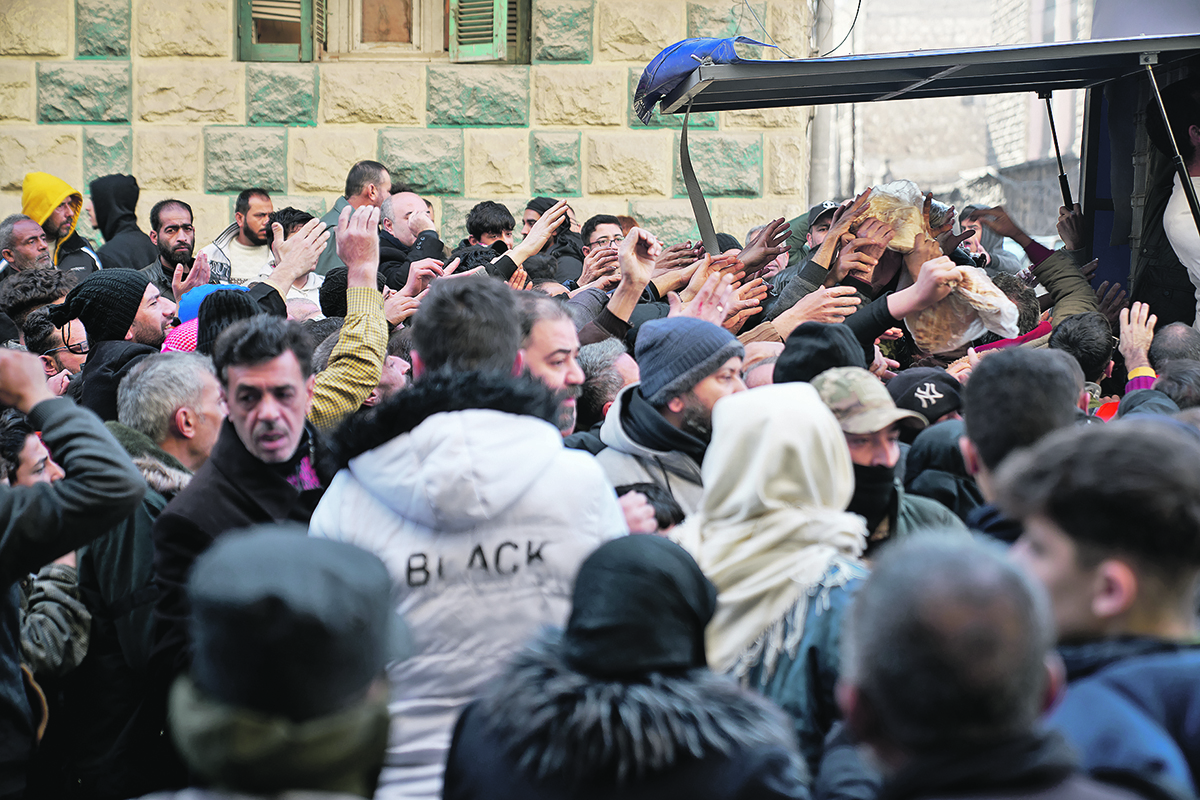 A crowd of people in Aleppo, Syria, push toward the back of a trailer, hands reaching into the air, trying to get some of the food being handed out.