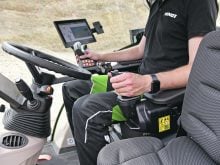 A man sits in the driver's seat of a modern Fendt tractor. There's a steering wheel in front of him, but his left hand is on a joystick.