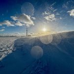 A low angle shot of snow blowing off a snow drift on a cold day with a blue sky and the sun low to the horizon.