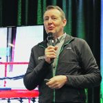 Tom Wolf speaks into a microphone during a presentation at the 2025 Crop Production Show in Saskatoon.