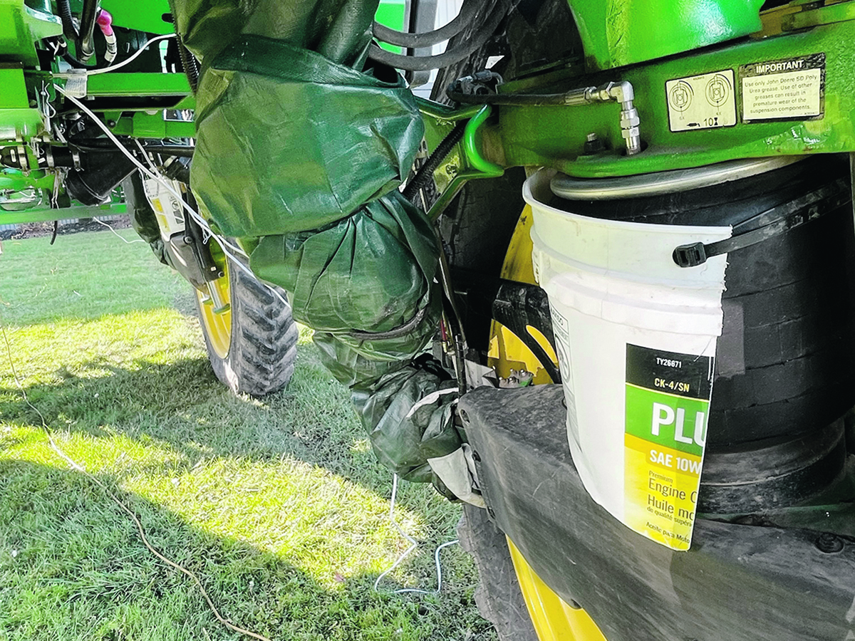 A photo of a plastic 5-gallon pail that has been cut in half and zip-tied to what looks like an air suspension bag on a piece of farm equipment to act as a protective cover.