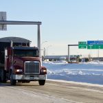 A grain truck with Manitoba plates drives on the highway near the U.S./Canada border.