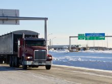 A grain truck with Manitoba plates drives on the highway near the U.S./Canada border.