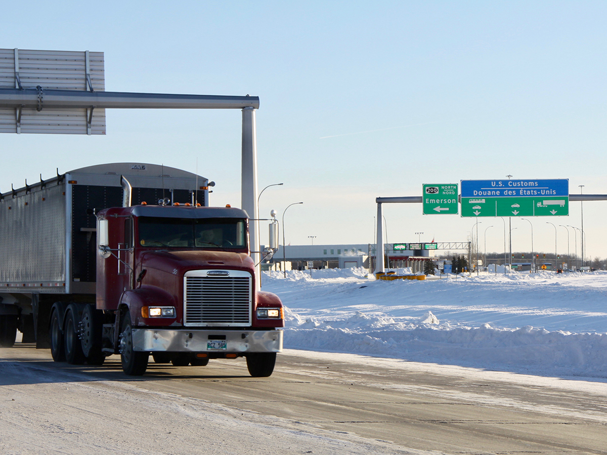 A grain truck with Manitoba plates drives on the highway near the U.S./Canada border.