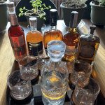 A variety of rye whisky bottles and glasses sit on a table.