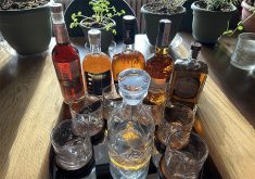 A variety of rye whisky bottles and glasses sit on a table.