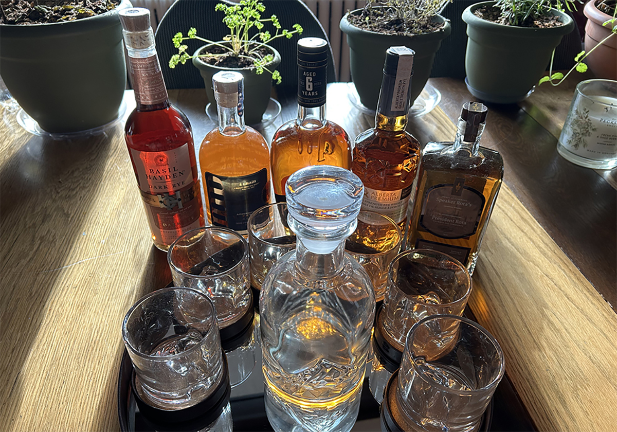 A variety of rye whisky bottles and glasses sit on a table.