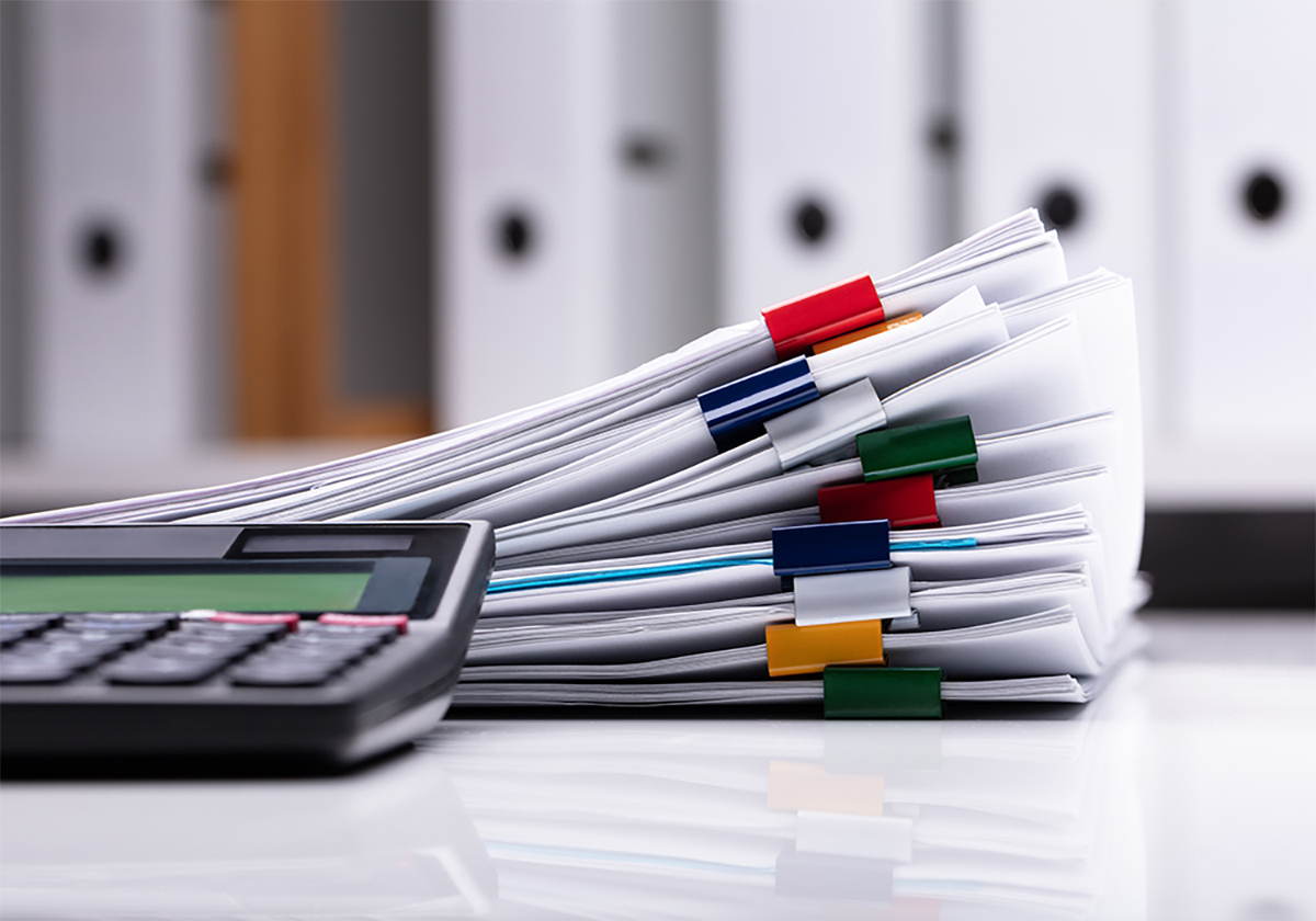 A stack of paperwork with a calculator off to the side.