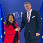 Canada's trade minister Mary Ng shakes hands with EU trade chief Maros Sefcovic in front of two European Union flags in the background.