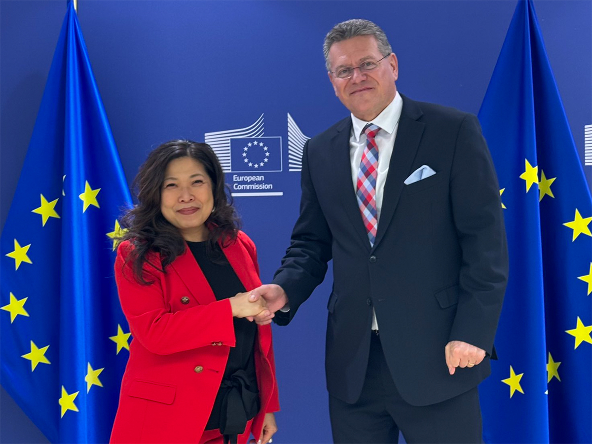 Canada's trade minister Mary Ng shakes hands with EU trade chief Maros Sefcovic in front of two European Union flags in the background.