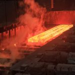A red hot piece of flat steel rolls along a conveyor in a steel factory.