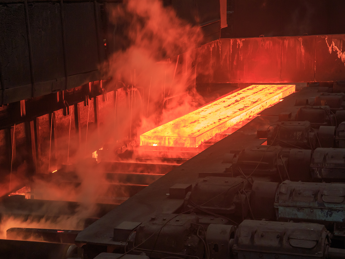 A red hot piece of flat steel rolls along a conveyor in a steel factory.