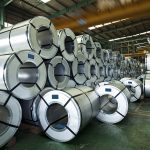 Rolls of shiny steel are stacked in a warehouse.