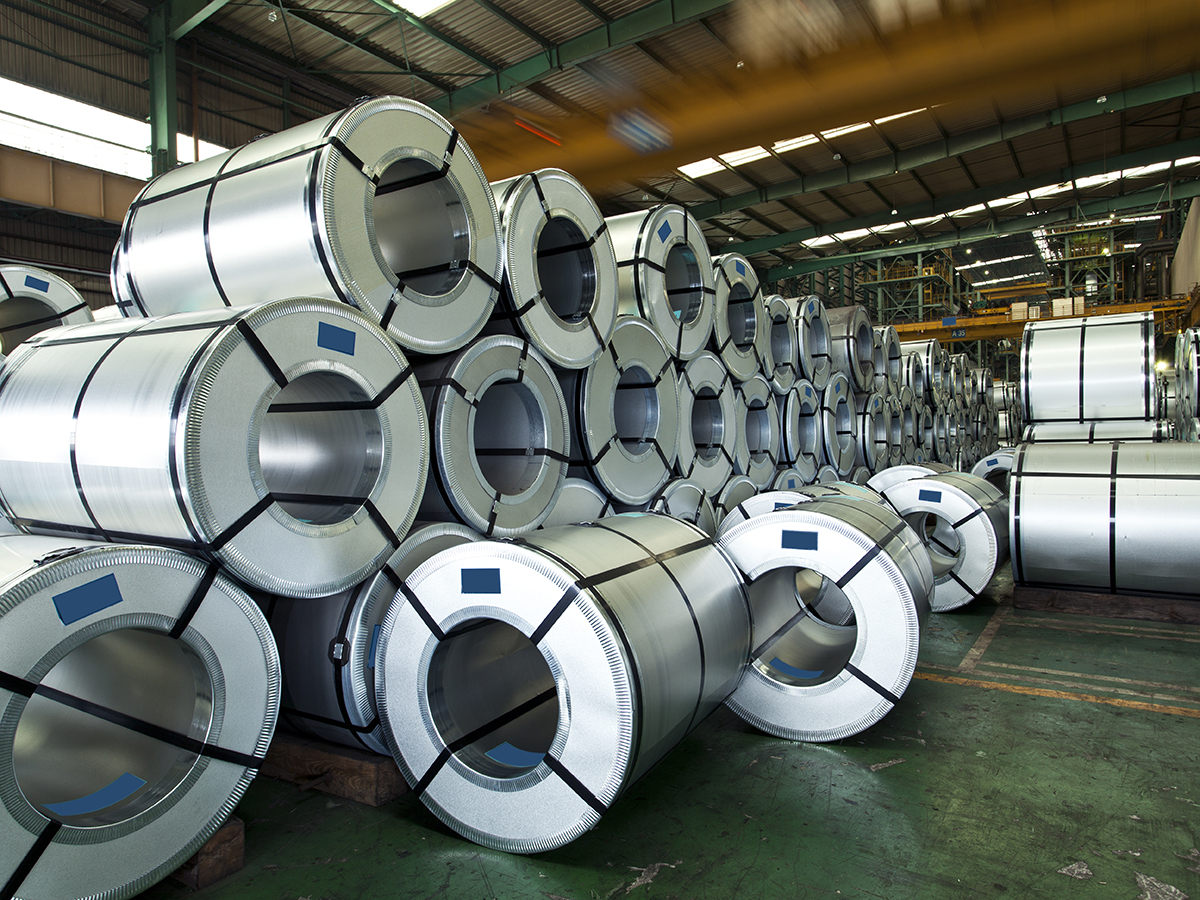Rolls of shiny steel are stacked in a warehouse.