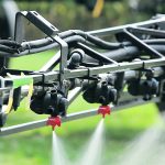 A close-up of a couple of nozzles with fluid coming out in a conical pattern on a sprayer arm.