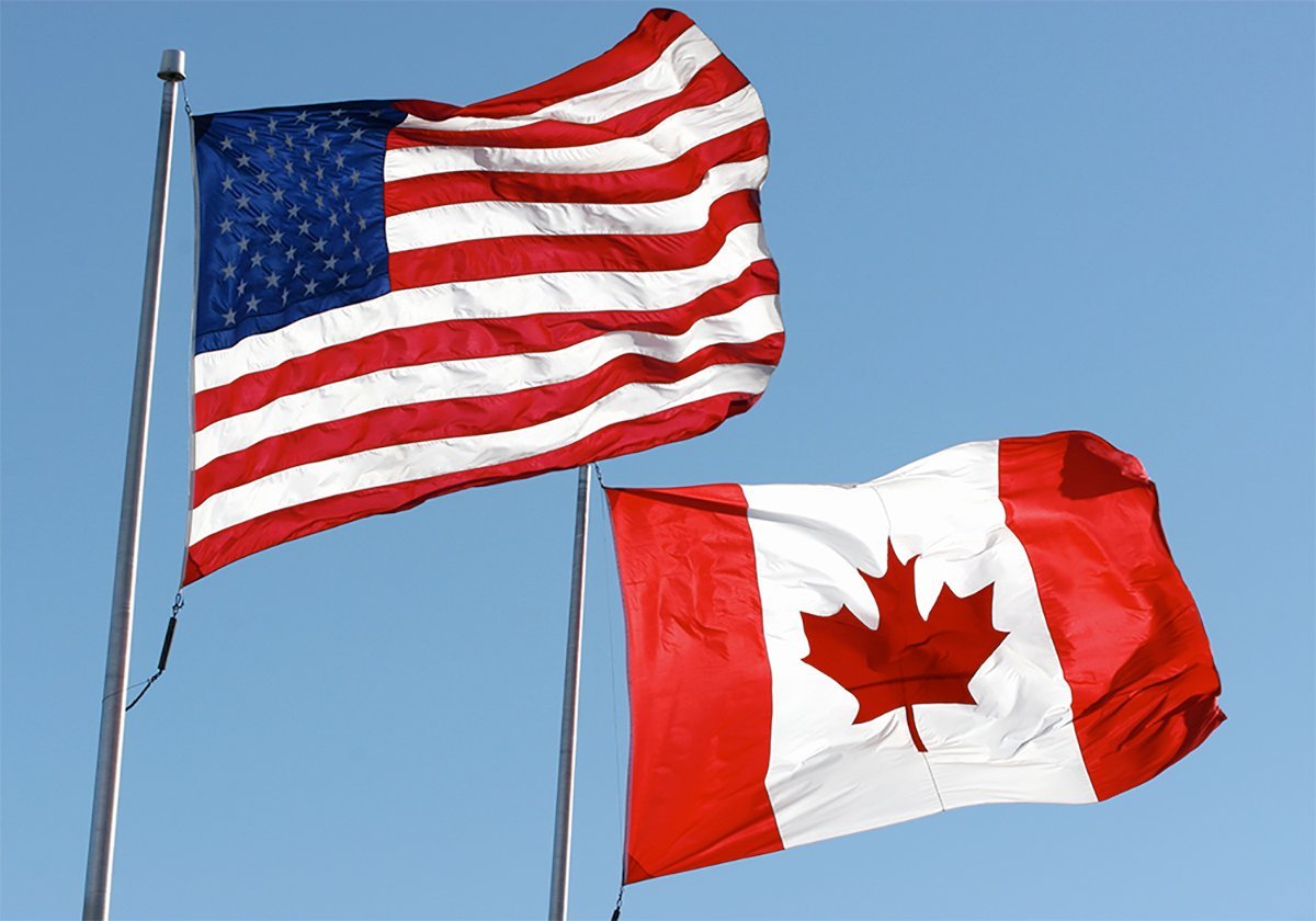 American and Canadian flags fly side-by-side against a clear blue sky background.