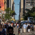 Hundreds of pedestrians walk along a street that has been closed to traffic to accommodate a street fair.