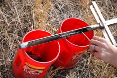 A soil probe rests on top of two red, 5-gallon pails in a field.