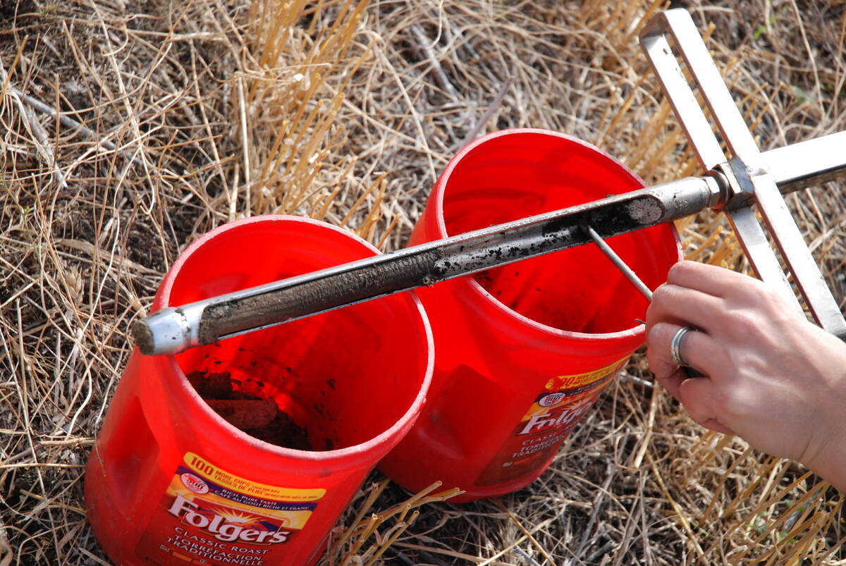 A soil probe rests on top of two red, 5-gallon pails in a field.