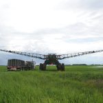 A large modern high-clearance sprayer is parked in a field next to its support truck.