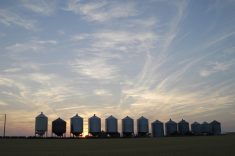 A row of steel grain bins with the sun setting behind them.