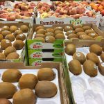 A variety of fruit, including kiwi fruit and peaches, sits in cases on display in a grocery story.
